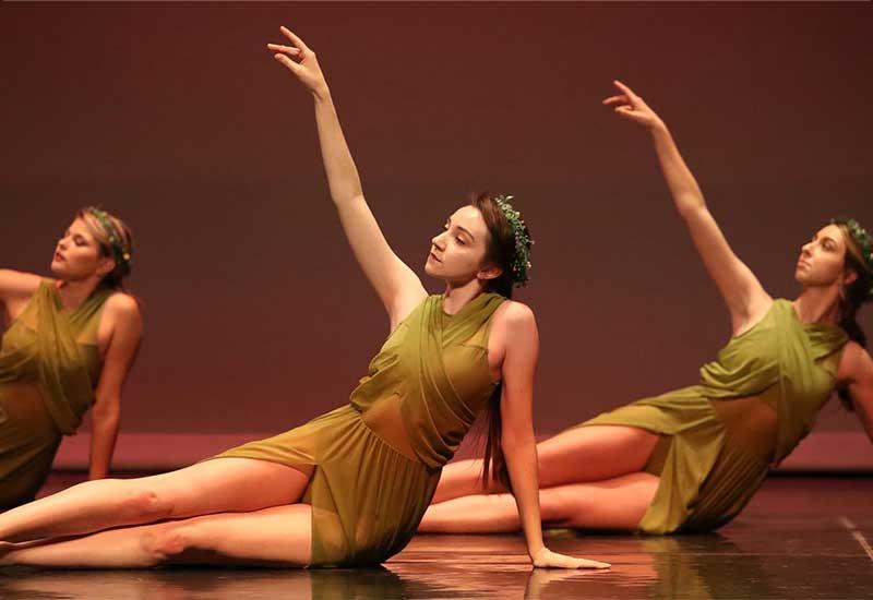 three students in green dresses perform a dance piece